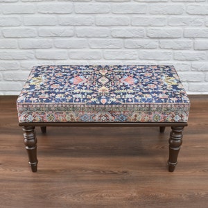 May include: A dark wood ottoman with a patterned fabric top. The fabric features a blue background with a colorful floral design.