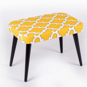May include: A yellow and white patterned ottoman with black wooden legs.