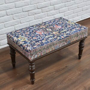 May include: A wooden bench with a dark blue and floral patterned cushion. The bench has four turned legs and a rectangular top.