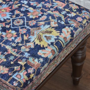May include: A dark blue upholstered ottoman with a traditional patterned fabric. The ottoman has four turned wooden legs.