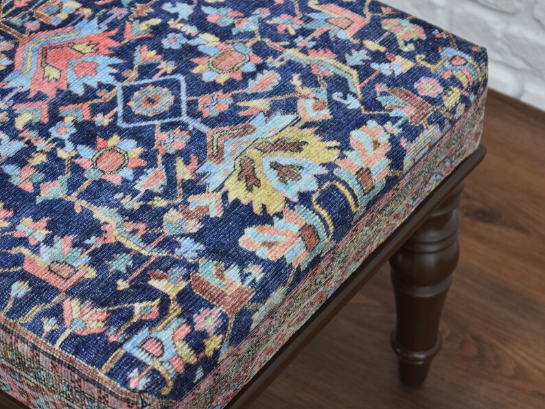 May include: A dark blue upholstered ottoman with a traditional patterned fabric. The ottoman has four turned wooden legs.