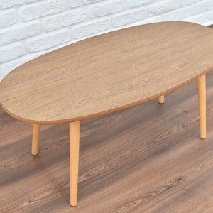 May include: A light brown oval-shaped coffee table with three wooden legs.
