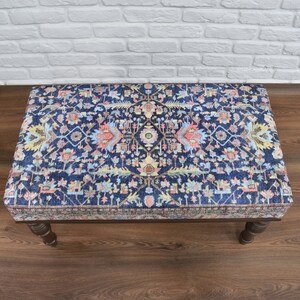 May include: A blue and pink patterned ottoman with wooden legs. The ottoman has a traditional design with intricate details.