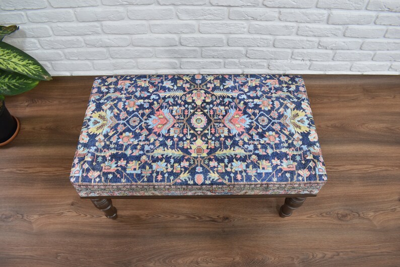 May include: A blue and pink patterned ottoman with wooden legs. The ottoman has a traditional design with intricate details.