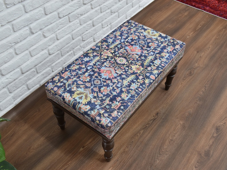 May include: A wooden ottoman with a dark blue and floral patterned fabric top. The ottoman has four legs and is sitting on a wooden floor.