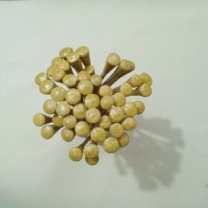 以下が含まれることがあります： 円形に扇状に配置された多数の薄茶色の木製ゴルフティーの束。各ティーは滑らかで丸いヘッドと先細りのシャフトを備えており、すべてが中心点に向かって集まり、密集した質感のある束を形成しています。