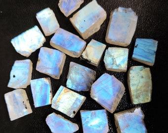 May include: A collection of iridescent rainbow moonstone rough pieces. The stones are various sizes and shapes, with a white base and a blue, green, and gold iridescent sheen.