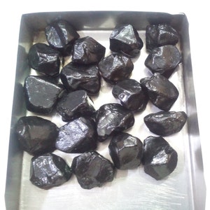 May include: A collection of black gemstones in a metal tray. The gemstones are various sizes and shapes, with a shiny, polished finish.
