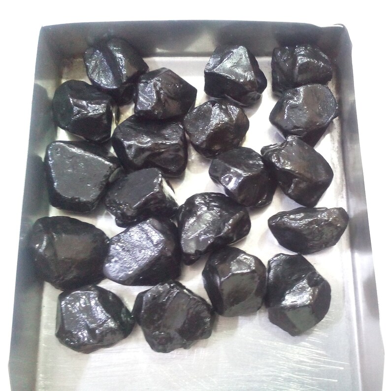 May include: A collection of black gemstones in a metal tray. The gemstones are various sizes and shapes, with a shiny, polished finish.