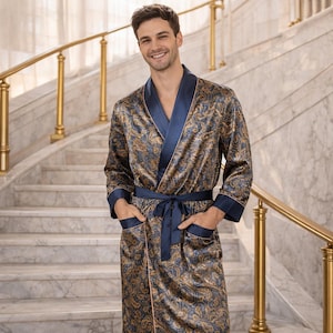May include: A patterned silk robe in shades of blue and gold. The robe features a shawl collar, a matching belt, and contrasting navy blue trim on the cuffs and pockets. The model is standing on a marble staircase.