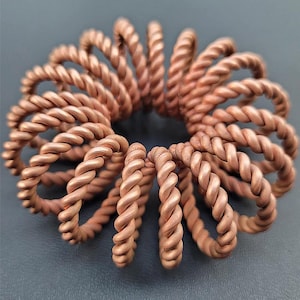 Könnte beinhalten: Nahaufnahme einer Gruppe von Kupferringen, die jeweils ein gedrehtes Seil-Design aufweisen. Die Ringe sind in einem kreisförmigen Muster angeordnet und bilden ein dekoratives und kompliziertes Design.