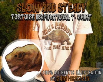 Op de afbeelding: Wit T-shirt met een bruine schildpad-illustratie en de tekst "Slow and Steady Wins the Race". De tekst is in een bruin, vintage-stijl lettertype. Het shirt wordt gedragen door een persoon.