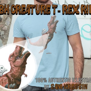 May include: A light blue t-shirt with a graphic of a Tyrannosaurus Rex carrying a small, white, round creature. The text "TBH CREATURE T-REX RIDE" is at the top of the shirt and "100% AUTHENTIC ILLUSTRATION BY SAM KRESSIN" is at the bottom.