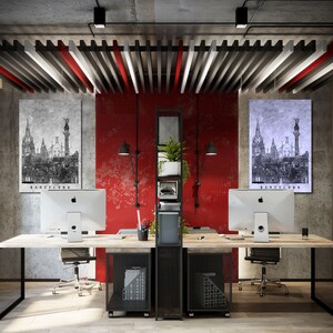 May include: Two black and white images of Barcelona, Spain, hang on a red wall in a modern office. Two desks with black metal frames and black mesh shelves are in the center of the room. Each desk has a silver computer monitor and a black office chair.