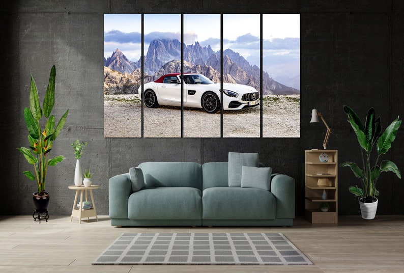 May include: A white convertible sports car with a red interior is parked on a dirt road in front of a mountain range. The car has a black roof and black wheels. The mountains are in the background and are covered in snow.