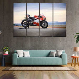 May include: A red and white sports motorcycle is parked on a gray asphalt track. The motorcycle has a black seat and black wheels. The background is a blurry image of a blue sky and green trees.