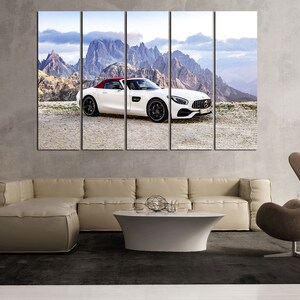 May include: A white convertible sports car with a red interior is parked on a mountain road with a view of snow-capped peaks in the background.