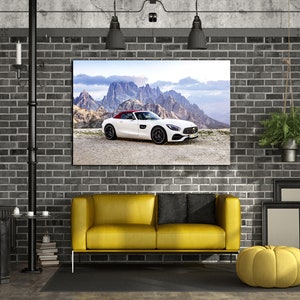 May include: A white convertible sports car with a red roof is featured in a framed print hanging on a brick wall. The print is above a yellow sofa with black pillows. The room is decorated in a modern industrial style with exposed brick and metal accents.