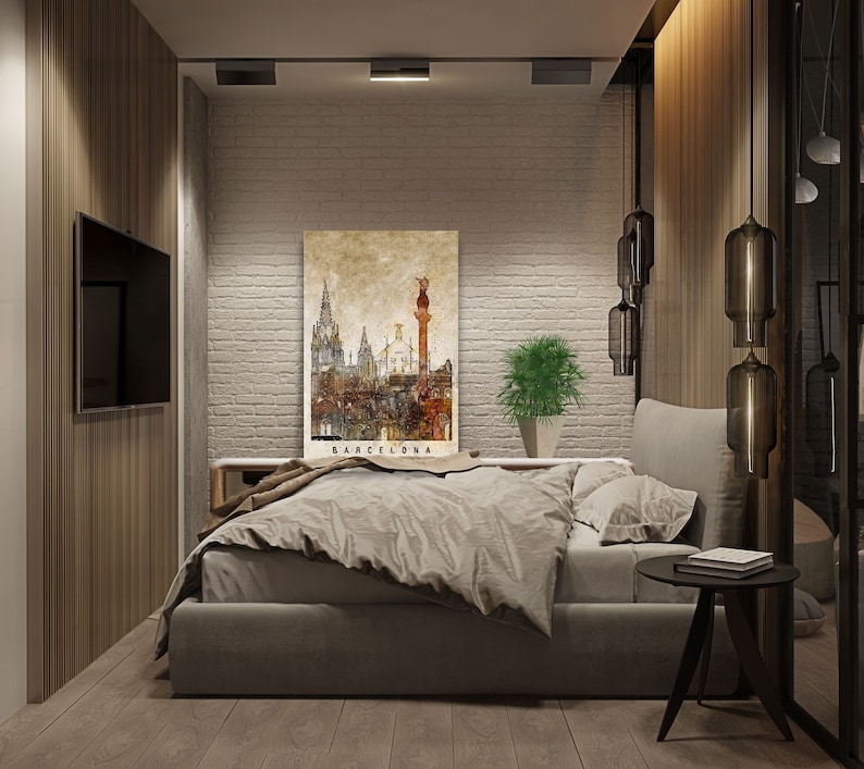 May include: A bedroom interior with a modern design featuring a bed with a gray duvet and pillows, a black side table, and a framed print of a cityscape with the word "Barcelona" at the bottom. The walls are white brick and the room has wood floors.