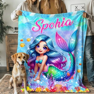 May include: A personalized mermaid-themed blanket with the name "Spohia" in pink script. The blanket features a cartoon mermaid with blue hair and a colorful tail, set against a blue ocean background with fish and coral.