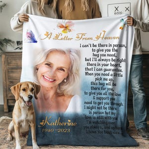 May include: A blue and white memorial blanket with a butterfly design and the text "A Letter From Heaven". The blanket features a photo of a woman with a warm smile and the text "Katherine 1940-2023".