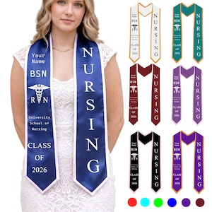 May include: A selection of graduation stoles in colours such as navy blue, white, maroon, teal, purple, and black. Each stole has the word "NURSING", the letters "BSN", and the year "2026". The stoles also display the "RVN" symbol and the words "University School of Nursing".