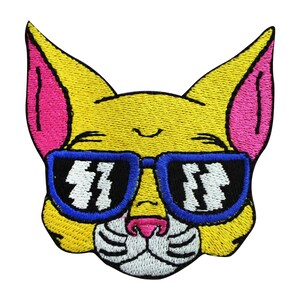 May include: Yellow cat face with pink ears wearing blue sunglasses with white lightning bolt designs. The cat has a white nose and whiskers.