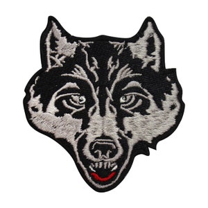 Op de afbeelding: Geborduurde patch met een wolfskop. De patch is voornamelijk zwart met grijze en witte details, die de gelaatstrekken van de wolf benadrukken. De bek van de wolf staat open en toont tanden en een rode tong. De patch is ontworpen om op stof te strijken of te naaien.