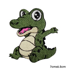Op de afbeelding: Groene geborduurde strijkpatch met een cartoon-alligator met grote ogen. De alligator zit met zijn bek open en zijn armen uitgestrekt. De patch is 7 cm bij 6,5 cm.