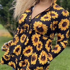 Op de afbeelding: Zwarte hoodie met een zonnebloemprint. De jas heeft een ritssluiting en een ruche detail op de taille.