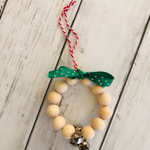 May include: A wooden bead wreath ornament with a green and white polka dot ribbon and silver bells. The wreath is strung on a red and white twine.