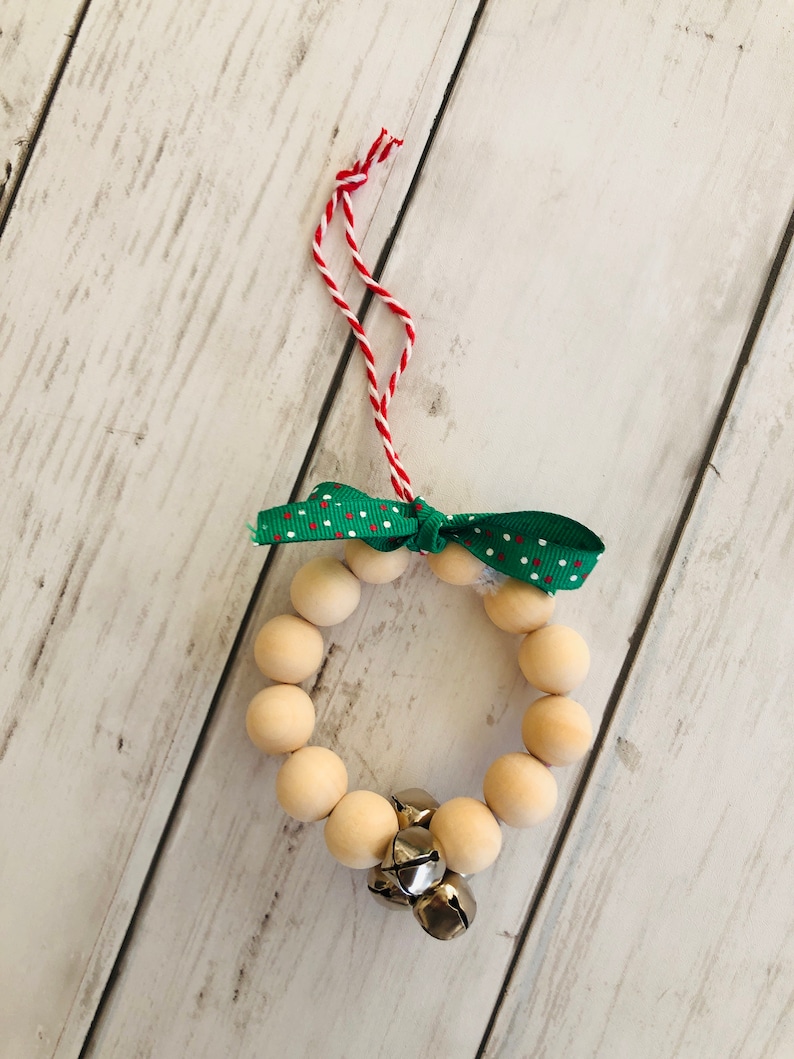 May include: A wooden bead wreath ornament with a green and white polka dot ribbon and silver bells. The wreath is strung on a red and white twine.