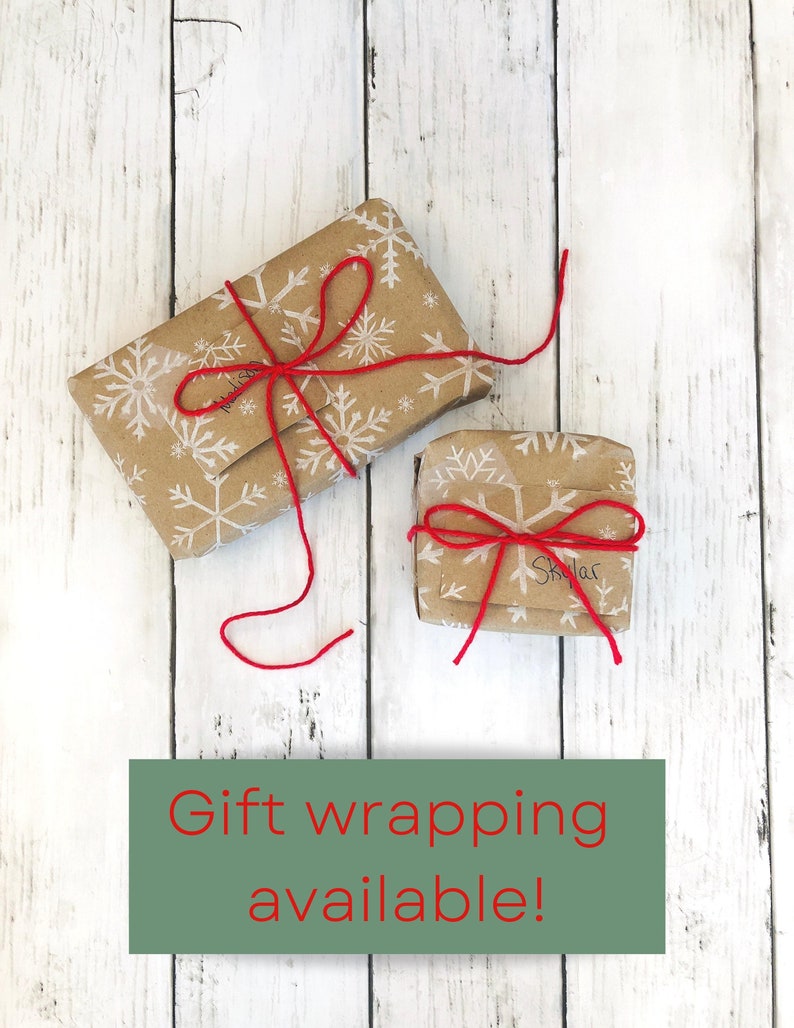 May include: Two small gifts wrapped in brown paper with white snowflakes printed on them. The gifts are tied with red string and bows. The text "Gift wrapping available!" is printed on a green rectangle below the gifts.