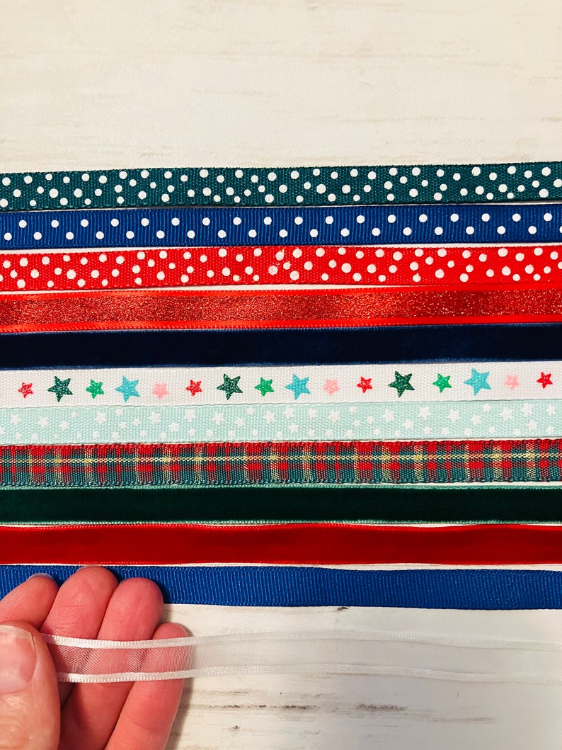 May include: Assortment of ribbon trims in various colors and patterns, including polka dots, stars, plaid, and velvet. The ribbons are arranged in rows on a white surface.