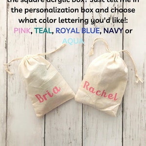 K&ouml;nnte beinhalten: Zwei wei&szlig;e Kordelbeutel mit den Namen "Bria" und "Rachel" in Pink darauf gedruckt. Die Beutel befinden sich auf einem hellen Holzhintergrund. Der Text "Prefer a personalized bag instead of the square acrylic box? Just tell me in the personalization box and choose what color lettering you'd like!: PINK, TEAL, ROYAL BLUE, NAVY or AQUA" befindet sich &uuml;ber den Beuteln.