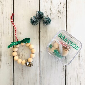 May include: A wooden bead wreath ornament kit with a green and white polka dot ribbon, bells, and a clear plastic container labeled "GRAYSON".
