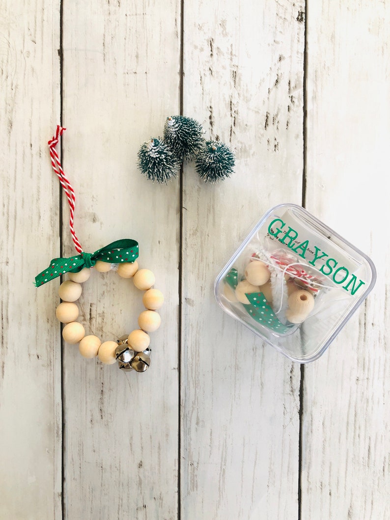 May include: A wooden bead wreath ornament kit with a green and white polka dot ribbon, bells, and a clear plastic container labeled "GRAYSON".