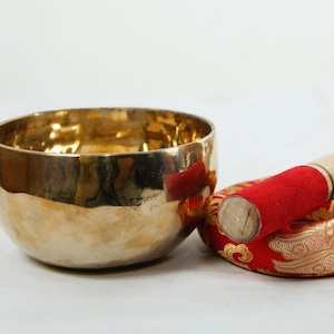 Puede incluir: Un cuenco cant&oacute;n dorado con un mazo de madera y un coj&iacute;n rojo con bordados dorados.