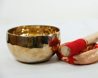 May include: A gold singing bowl with a wooden striker and a red cushion with gold embroidery.