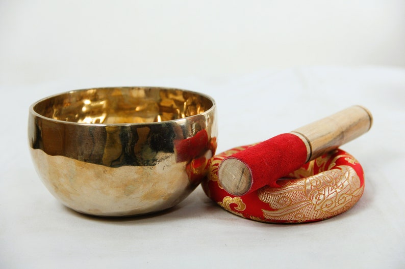 Puede incluir: Un cuenco cant&oacute;n dorado con un mazo de madera y un coj&iacute;n rojo con bordados dorados.