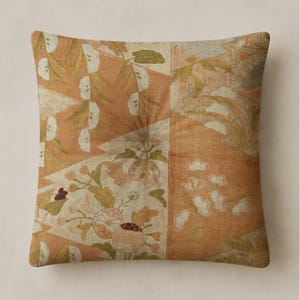 Puede incluir: Cojín decorativo cuadrado con diseño de patchwork. El cojín presenta un estampado floral en tonos naranja, crema y verde. El diseño incluye flores, hojas y formas geométricas, creando una estética vintage.