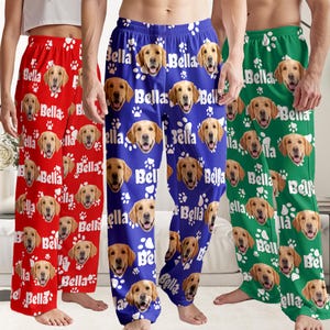 May include: Three pairs of pajama pants in red, blue, and green, each featuring a repeating pattern of a golden retriever's face, paw prints, and the name "Bella" in white. The pants have a relaxed fit.