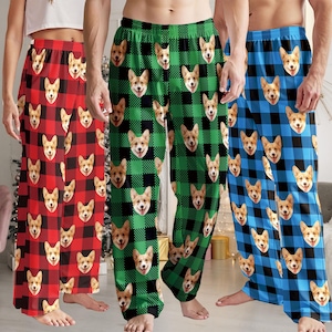 May include: Three pairs of pajama pants in red, green, and blue plaid patterns. Each pair features a repeating pattern of a corgi's face. The pants are loose-fitting and appear to be made of a soft material.