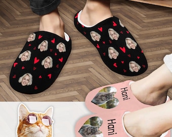 May include: Two pairs of personalized slippers. One pair is black with a repeating pattern of red hearts and a woman's face. The other pair is pink with a cat's face and the name "Hani" on each slipper.