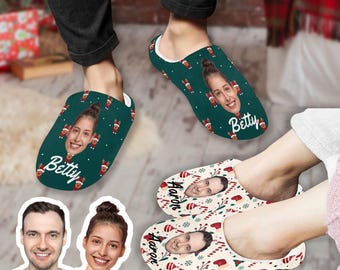 May include: A pair of personalized Christmas slippers with a green and red design. The slippers feature a person's face and the name "Betty" on one slipper and the name "Aaron" on the other slipper.