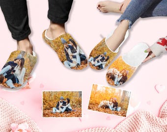 May include: A pair of white slippers with a photo printed on the top. The photo shows a couple in a fall setting with a dog. The slippers are on a pink surface with a white blanket.