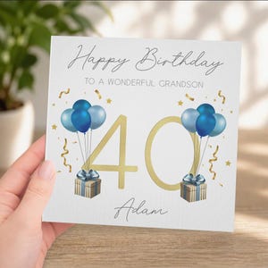 Peut inclure: Carte de joyeux anniversaire blanche avec le texte "Happy Birthday To A Wonderful Grandson". La carte présente des ballons bleus, des confettis dorés et un "40" doré. Deux coffrets cadeaux avec des rubans bleus sont également présents.