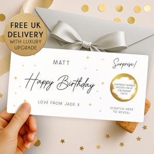 May include: A birthday card with a white background, gold stars, and the words "Happy Birthday". The card has a scratch-off area for a surprise, a grey envelope, and a silver bow. The text reads "Overnight Murder Mystery Stay at Chillingham Castle".