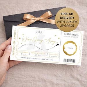 May include: A gold and white travel ticket design with the words "We're Going Away". The ticket includes the passenger's name, departure date, and destination. The background features a dark grey envelope and a gold ribbon.