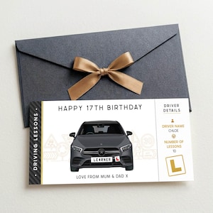 May include: A rectangular gift voucher for driving lessons featuring a dark grey car illustration, the text HAPPY 17TH BIRTHDAY, and a driver details section for Chloe with 10 lessons. The voucher is placed below a dark grey envelope with a gold ribbon.